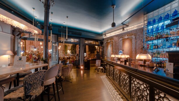 A bar area with a long counter, bar stools, and a patterned railing. - Xenon Inn (Nafplio)