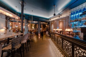 A bar area with a long counter, bar stools, and a patterned railing. - Xenon Inn (Nafplio)