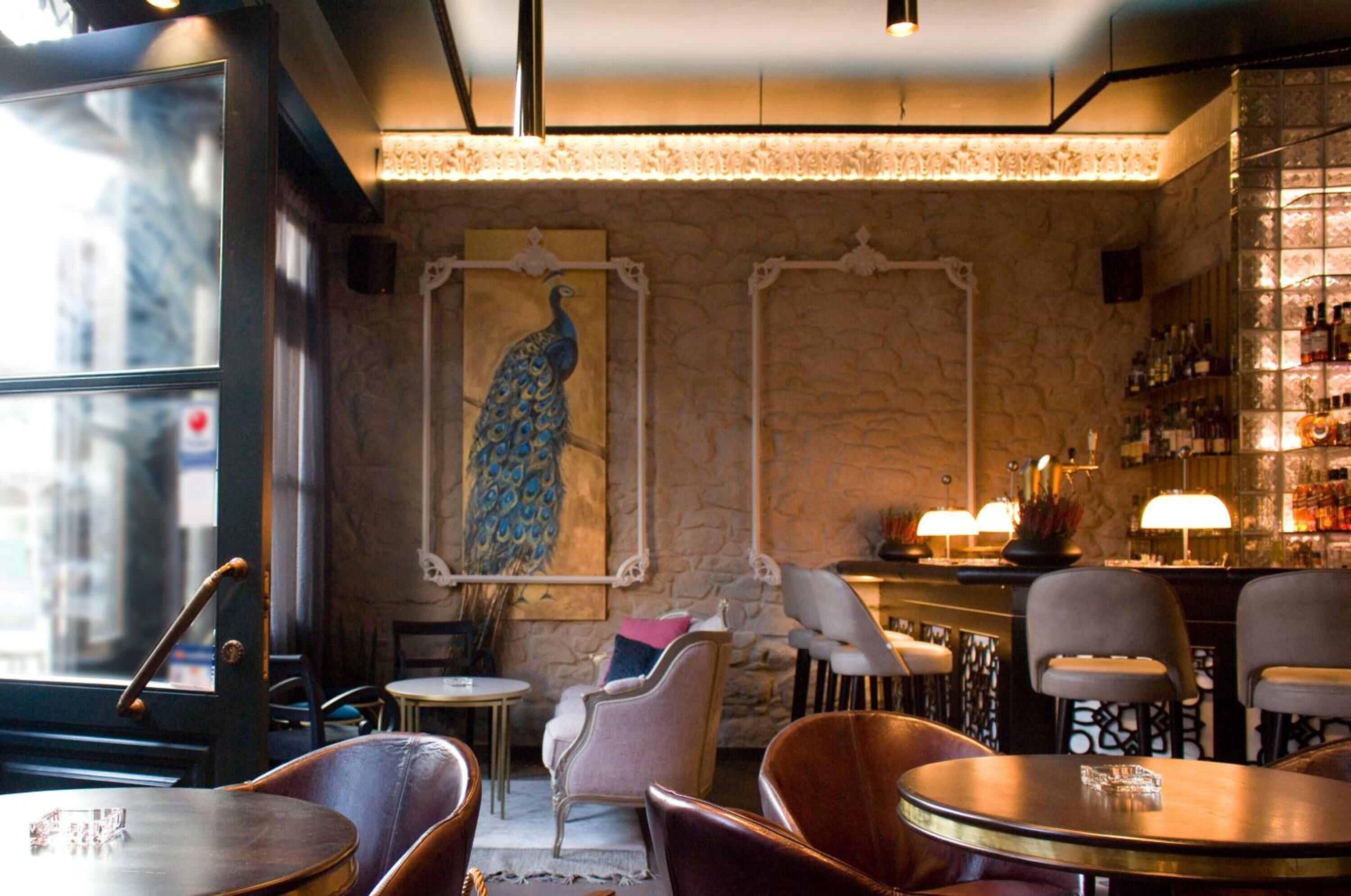 A cozy bar area with stone walls, a peacock painting, and a variety of seating options including chairs and tables.