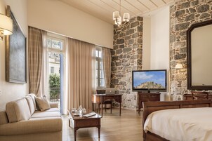 Habitación de hotel con pared de piedra, cama, sofá, escritorio con una computadora portátil, televisor y balcón con cortinas.
