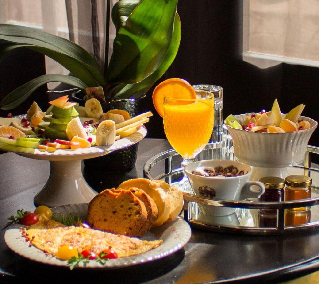 A breakfast tray with various foods including fruits, a glass of orange juice, and a bowl of cereal.
