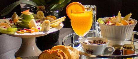 A breakfast tray with various foods including fruits, a glass of orange juice, and a bowl of cereal.