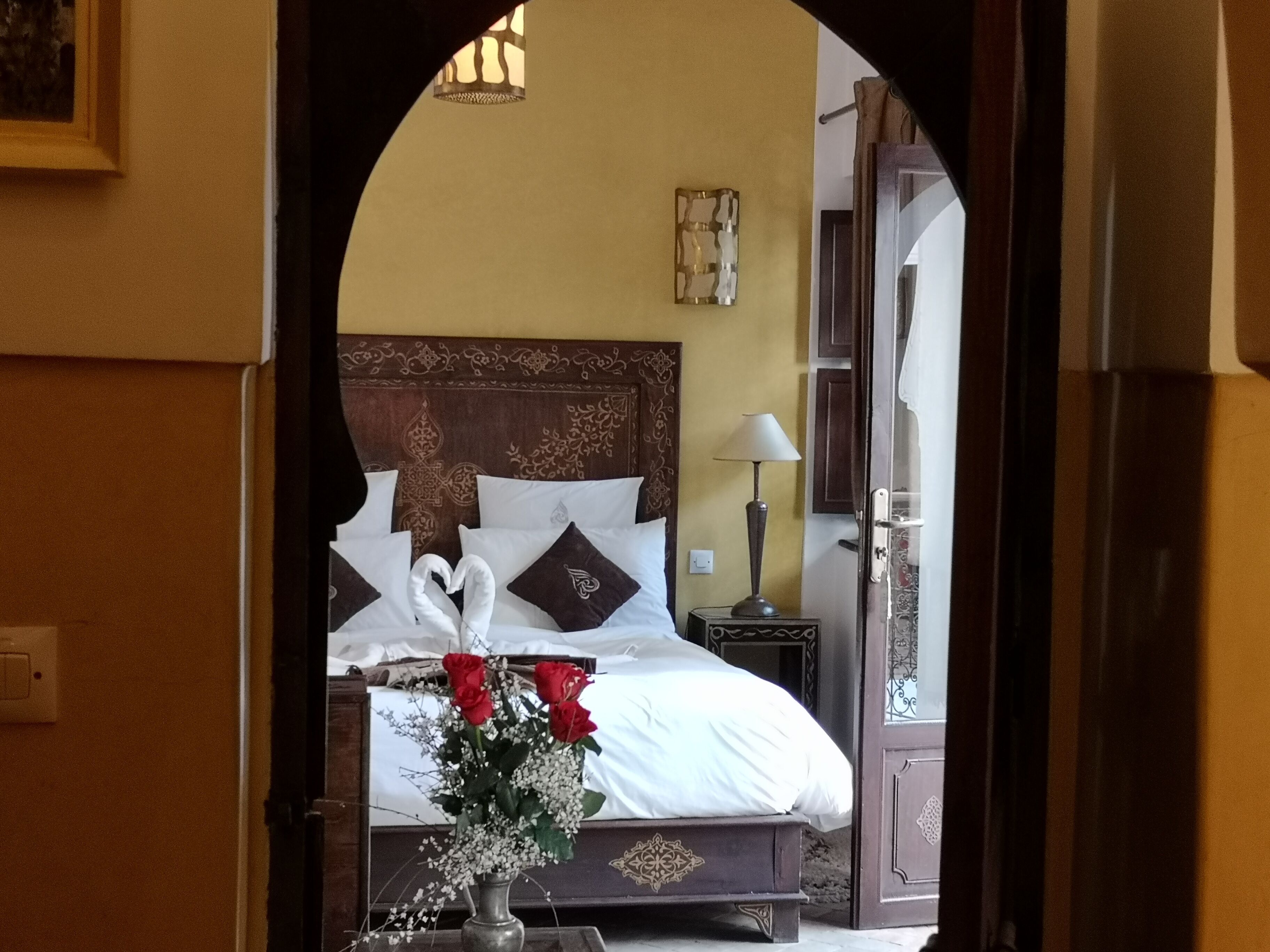 A hotel room with a bed, a nightstand, a lamp, and a vase with flowers.