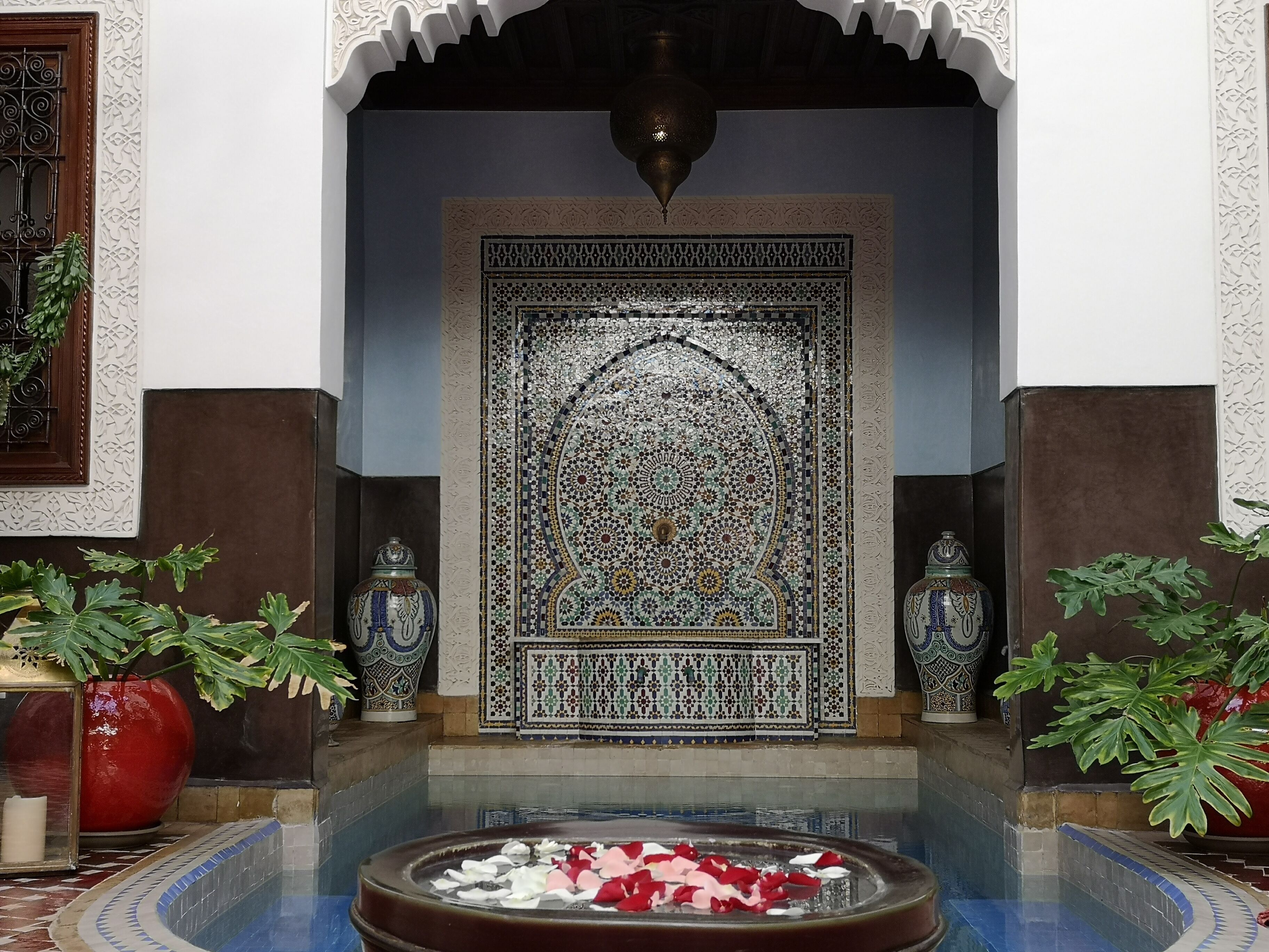 An ornate entrance with a fountain, decorative tiles, and potted plants.