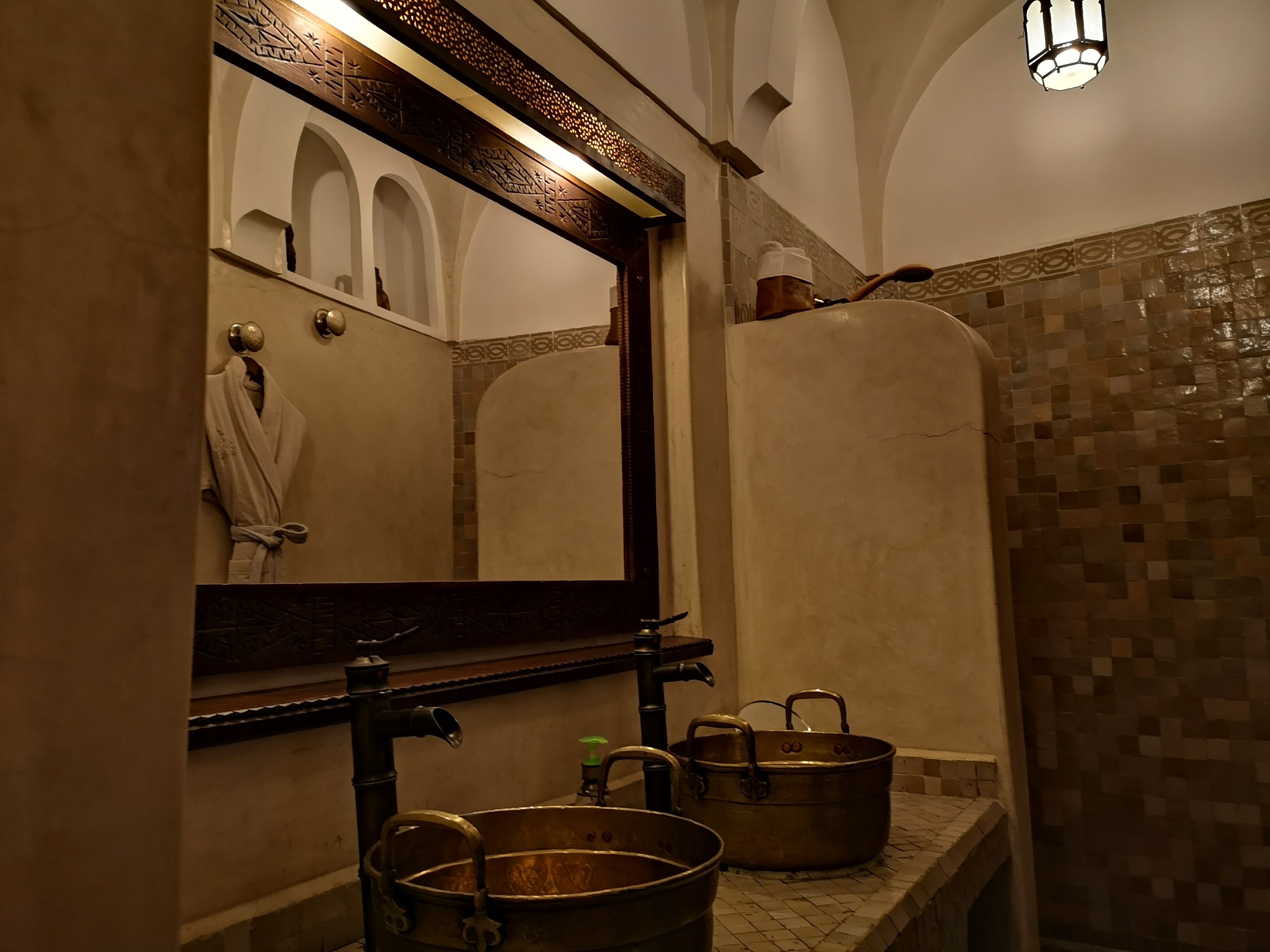 A bathroom with a large mirror, a sink with a metal basin, and a tiled shower area.