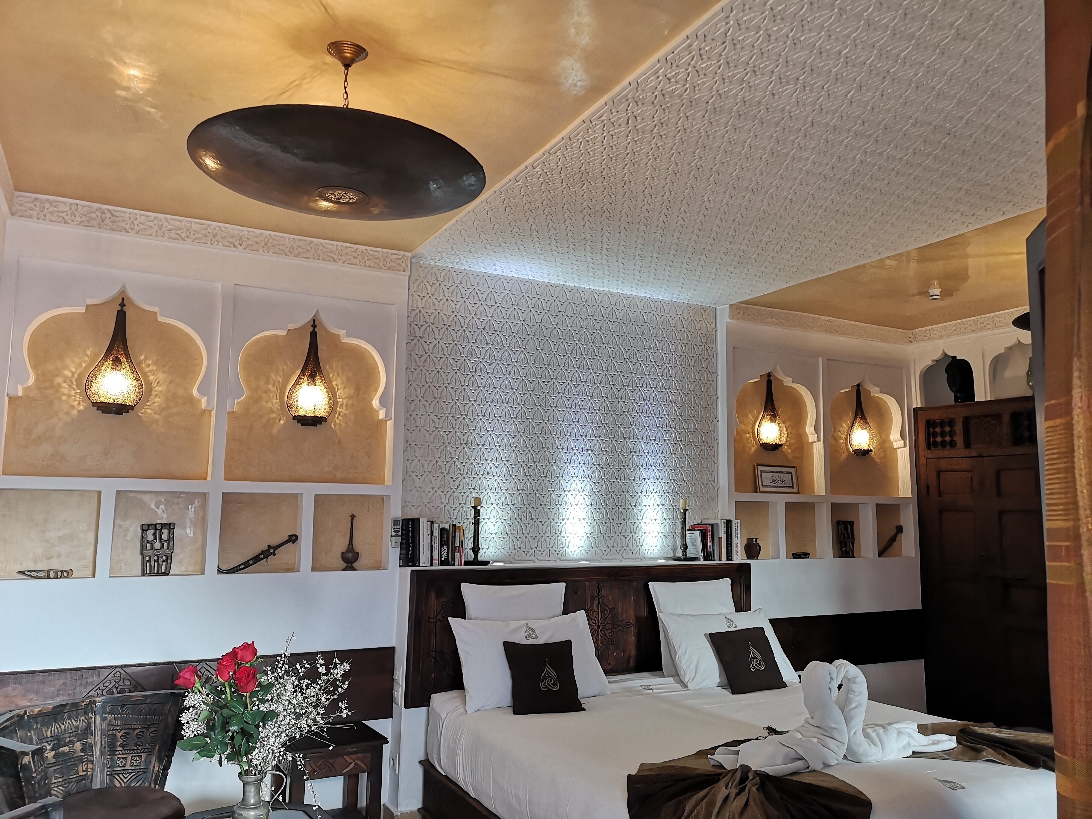 A hotel room with a large bed, decorative wall shelves, and hanging light fixtures.
