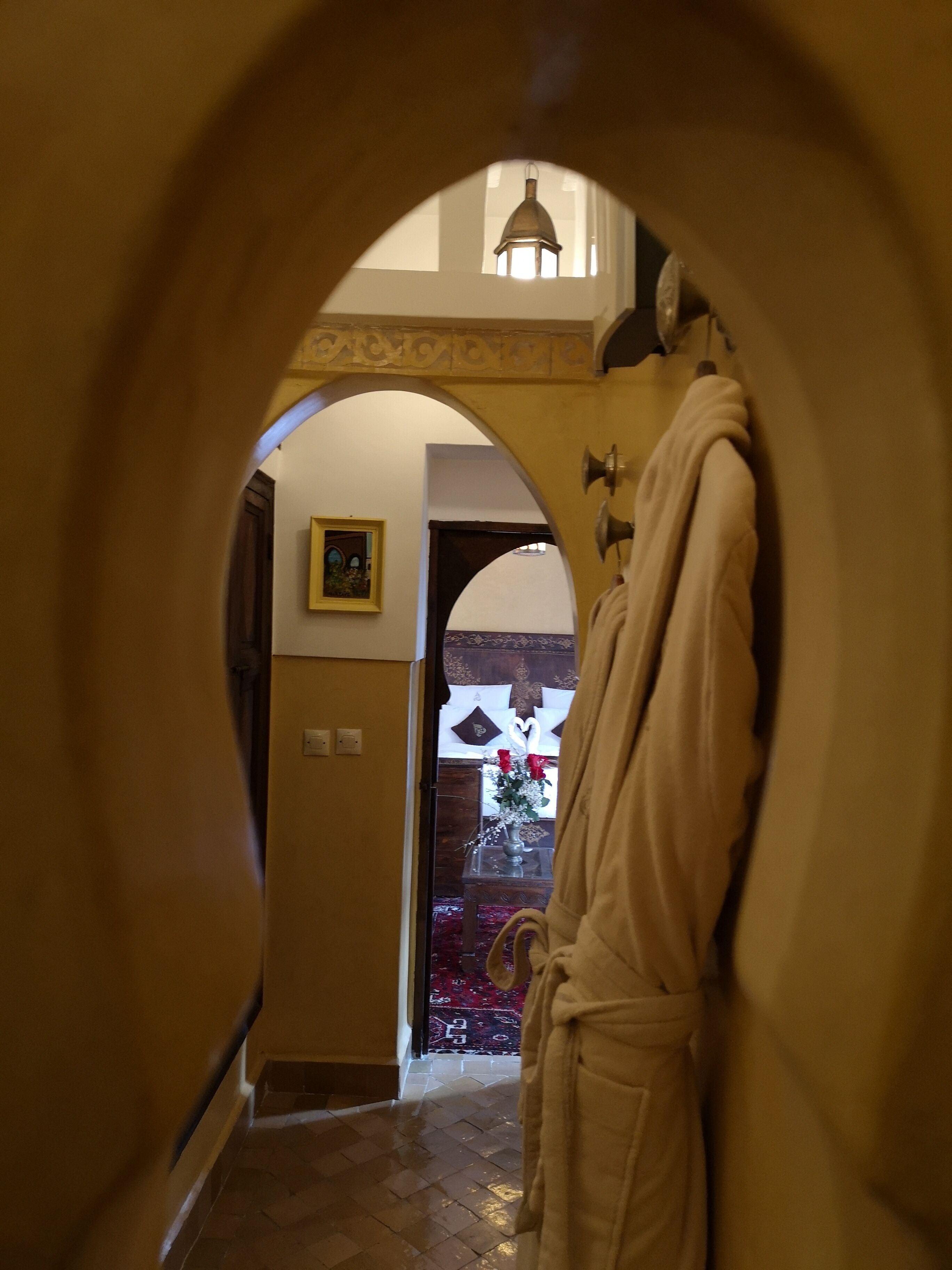 A hallway with an arched doorway leading to a room. A robe hangs on the wall, and a framed picture is visible on the wall.