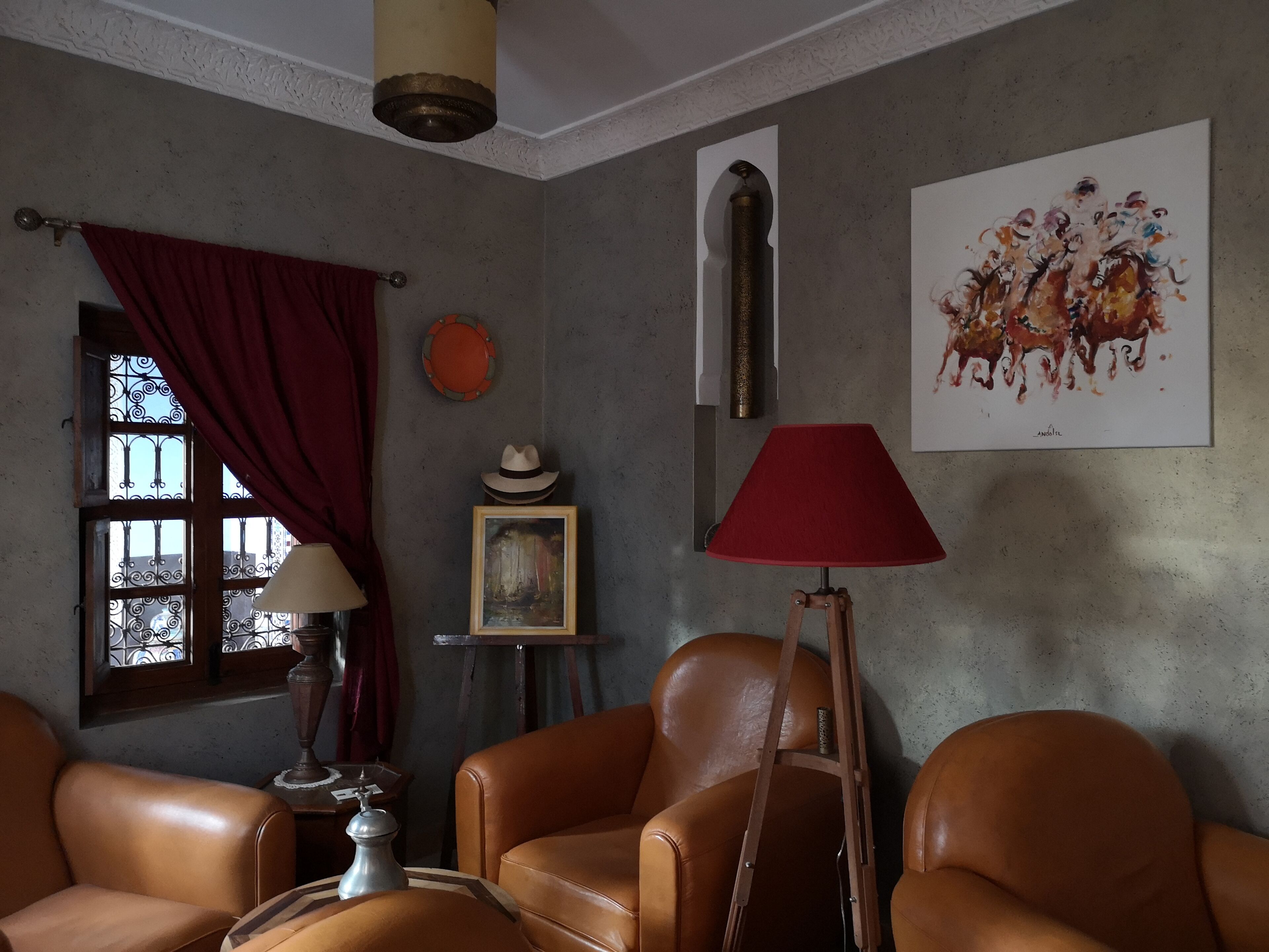 A room with leather chairs, a red lamp, a painting, and a decorative wall piece.