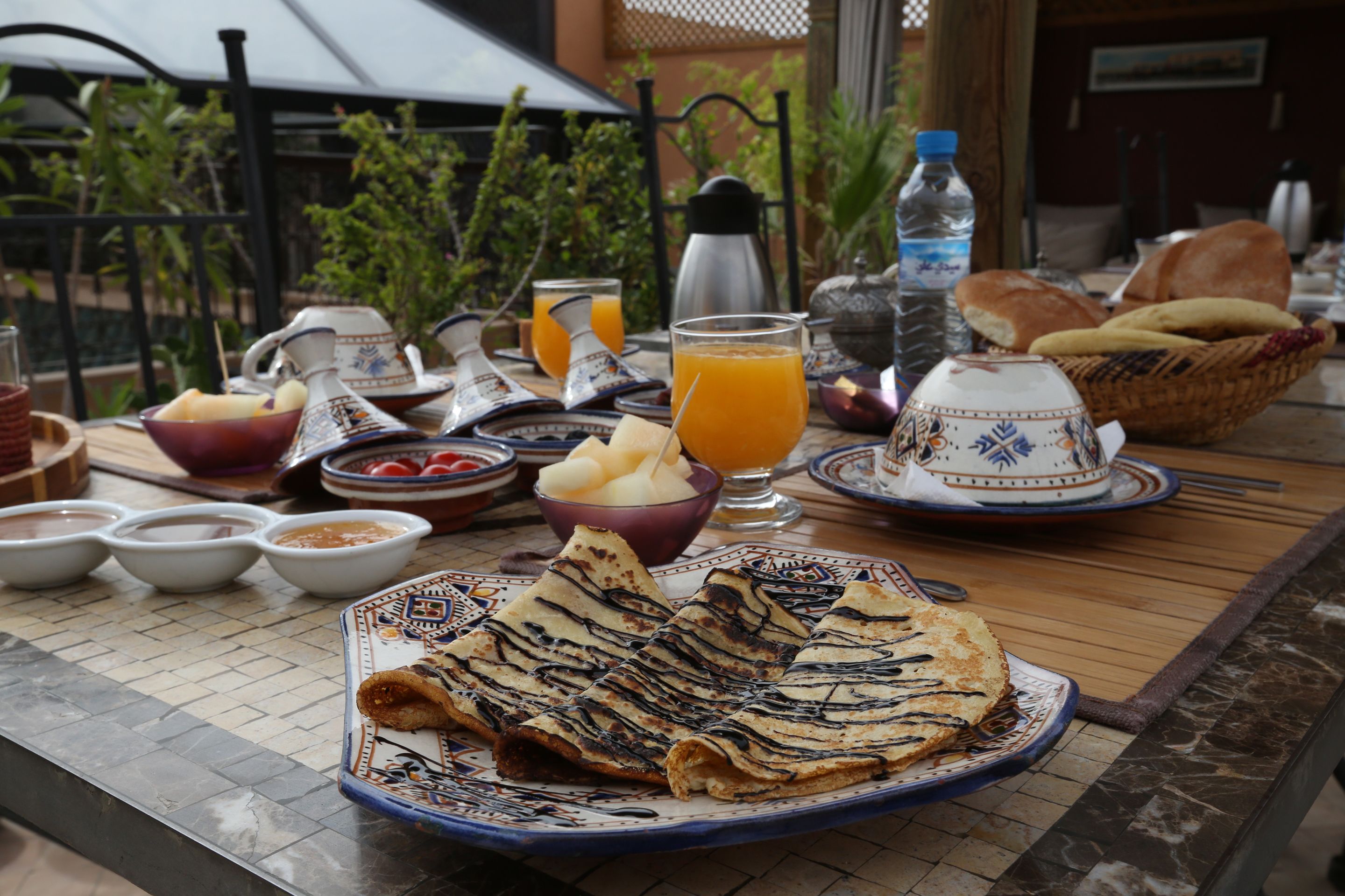 A breakfast table with various dishes, including crepes, fruit, and beverages.