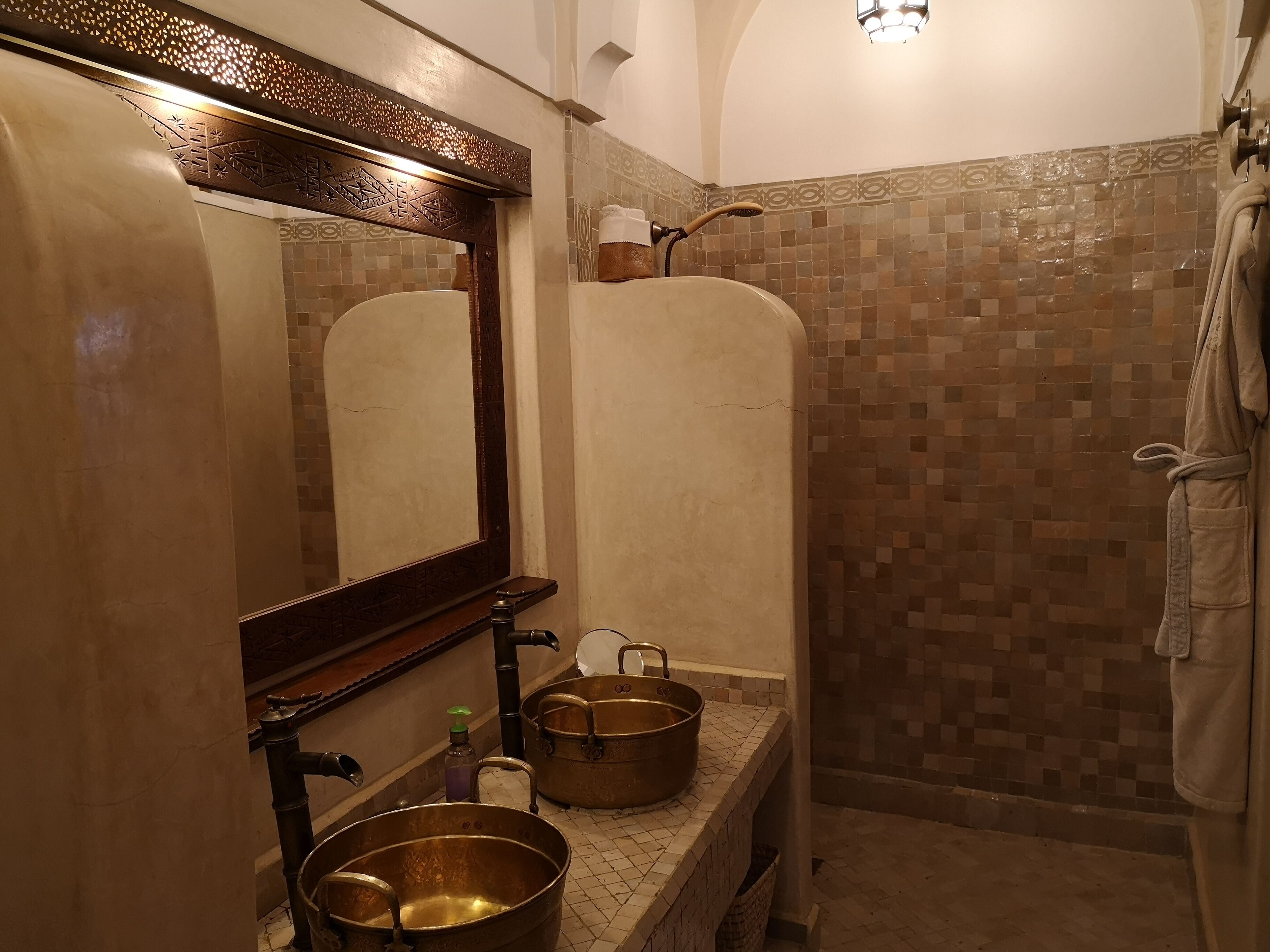A bathroom with a large mirror, two sinks, a shower, and a tiled wall.