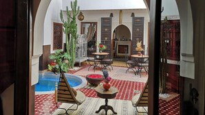 Ein offener Innenhof mit Pool, Sitzbereichen und Blick auf den oberen Stock durch einen Bogen.