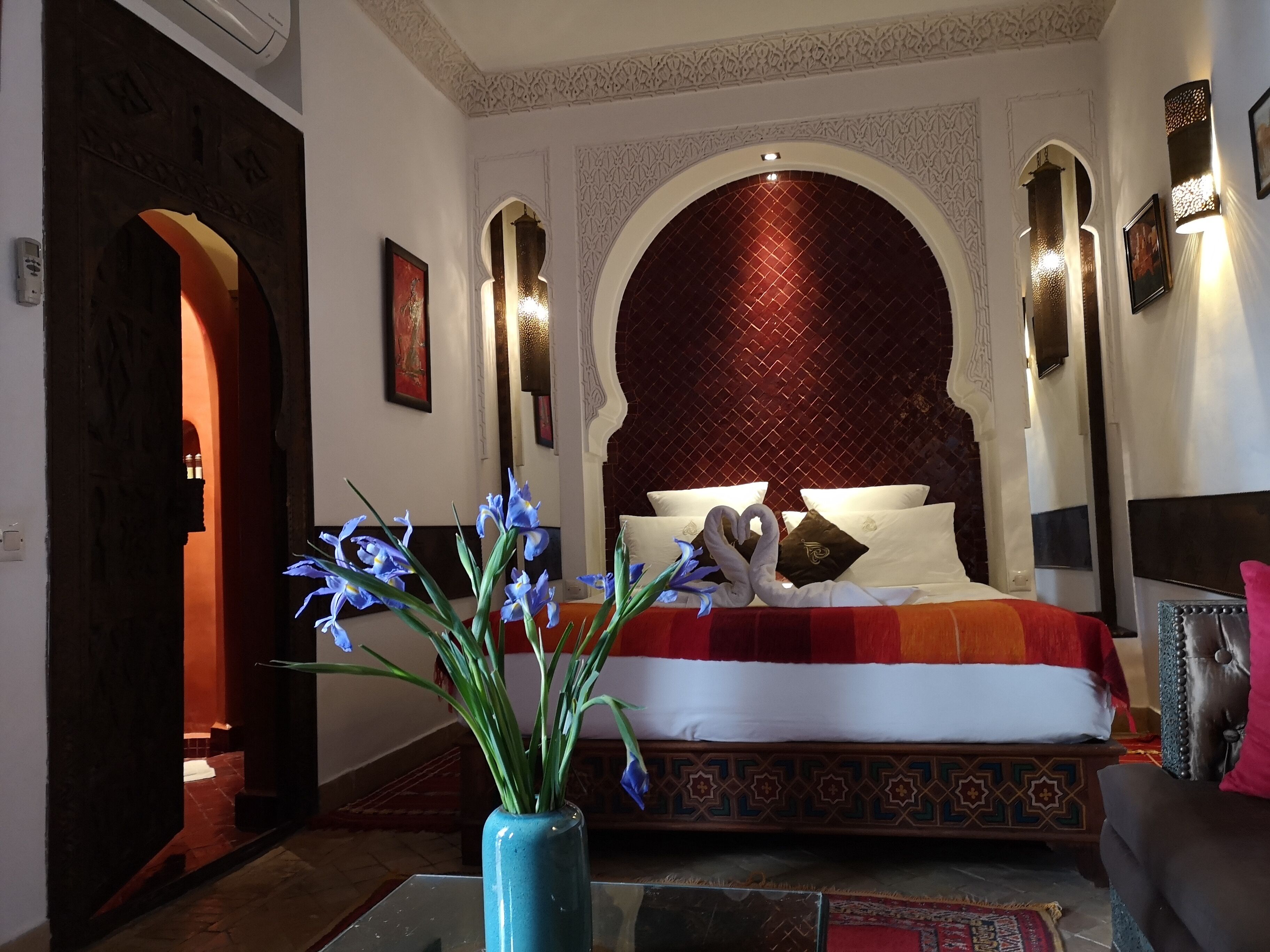 A hotel room with a large bed, ornate wall arches, and a decorative vase with flowers.