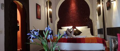 A hotel room with a large bed, ornate wall arches, and a decorative vase with flowers.