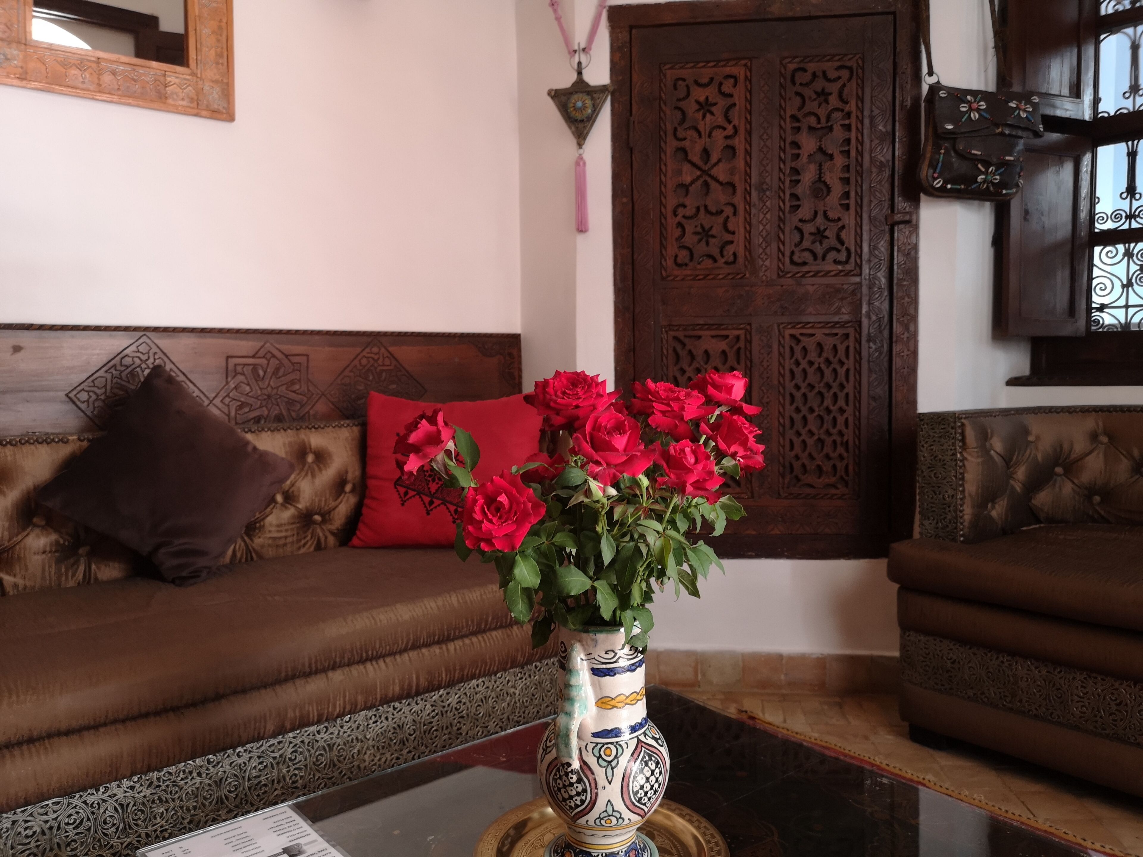 A living room with a brown sofa, a red cushion, and a vase with red flowers on a table.