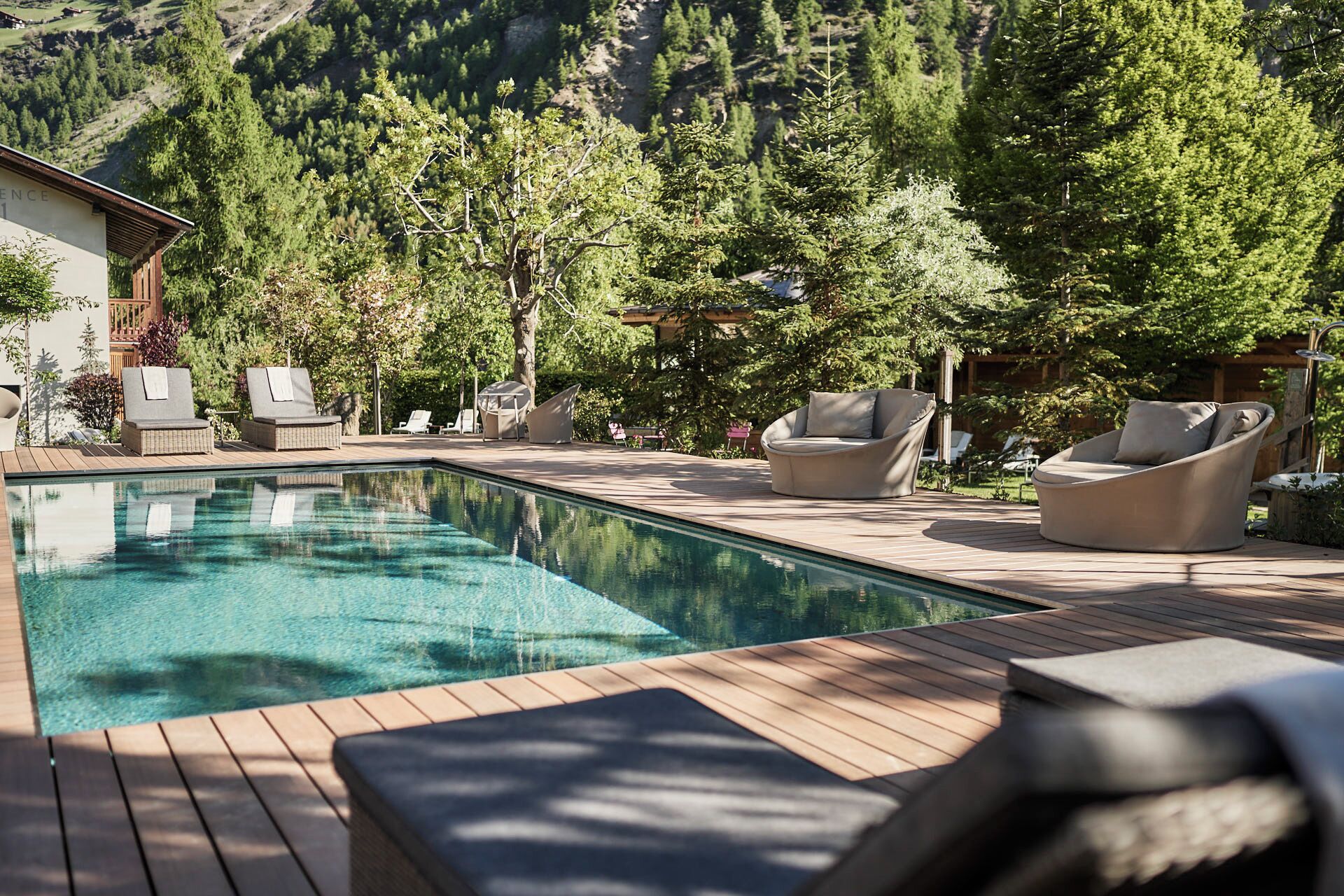 A pool area with wooden decking, lounge chairs, and a mountain backdrop.