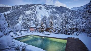Schneebedeckte Landschaft mit Schwimmbecken und Holzterrasse.