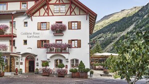 A traditional Alpine-style building with a white facade, red wooden beams, and multiple flower boxes. - Goldene Rose Karthaus (Senales)