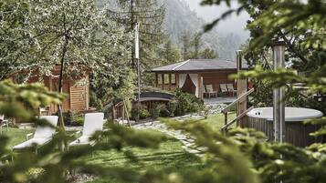 Eine Holzhütte mit Whirlpool, Liegestühlen und einer überdachten Terrasse, umgeben von Bäumen und Bergen.