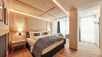 Ein modernes Hotelzimmer mit Holzboden, einem großen Bett mit gemusterten Textilien, einem Nachttisch mit Lampe und Blick auf einen Balkon mit Vorhängen.