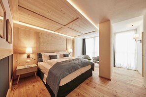 A modern hotel room with a wooden ceiling, a large bed with patterned bedding, a bedside table with a lamp, and a view of a balcony with curtains.