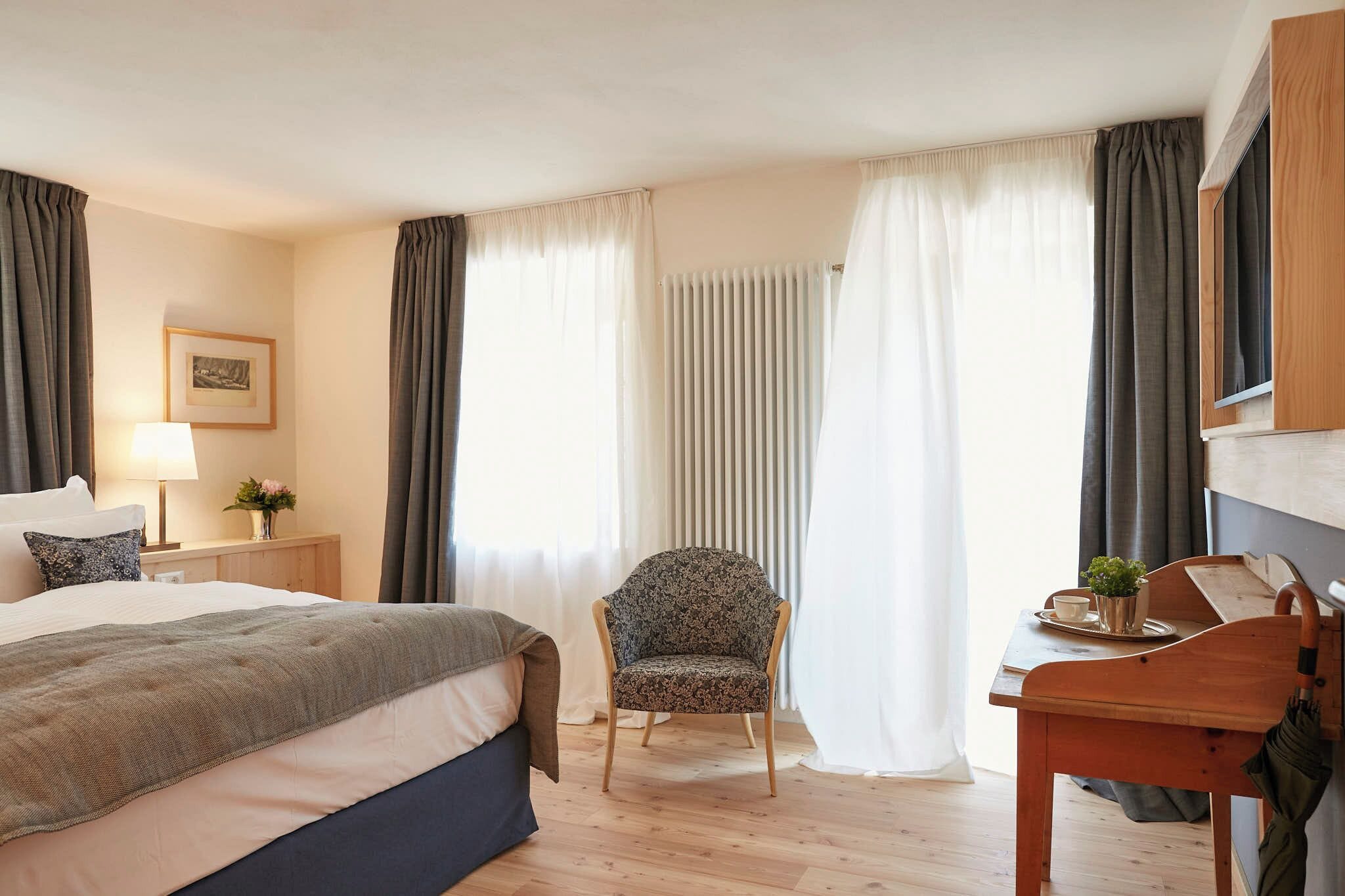 A hotel room with a bed, a chair, a table with a tray, a lamp, a picture on the wall, and a window with curtains.