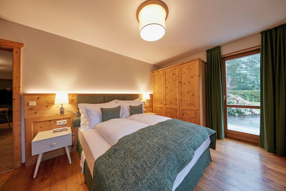 Une chambre à coucher avec une tête de lit en bois, un lit recouvert de draps blancs, une table de chevet et une fenêtre avec des rideaux.