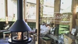 A glass door with a fireplace and a person relaxing on a bench. - Goldene Rose Karthaus (Senales)