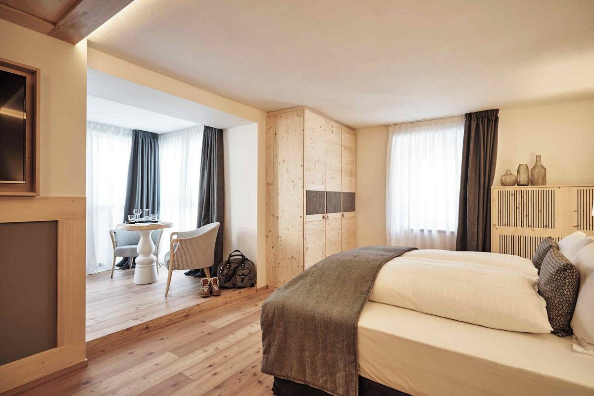 Une chambre d’hôtel avec une armoire en bois, un lit avec une couverture, une petite table avec des chaises et une vue sur l’extérieur par une fenêtre.