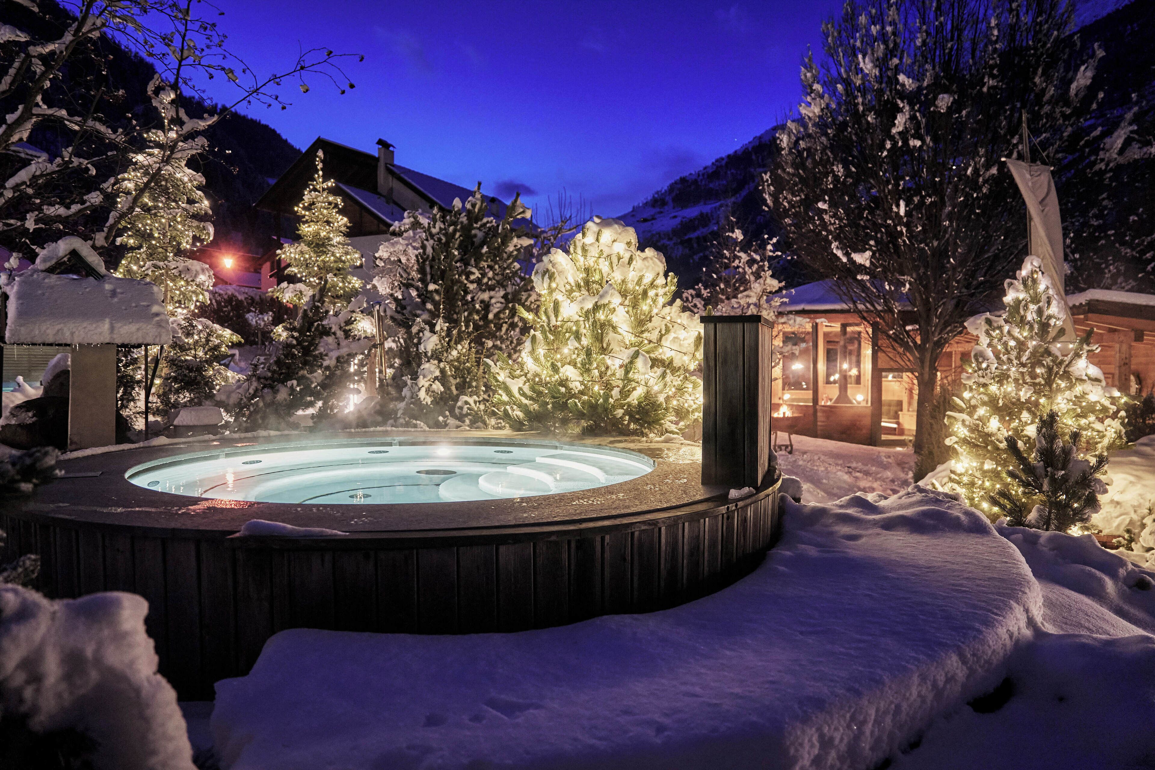 A hot tub surrounded by snow-covered trees and a wooden cabin.