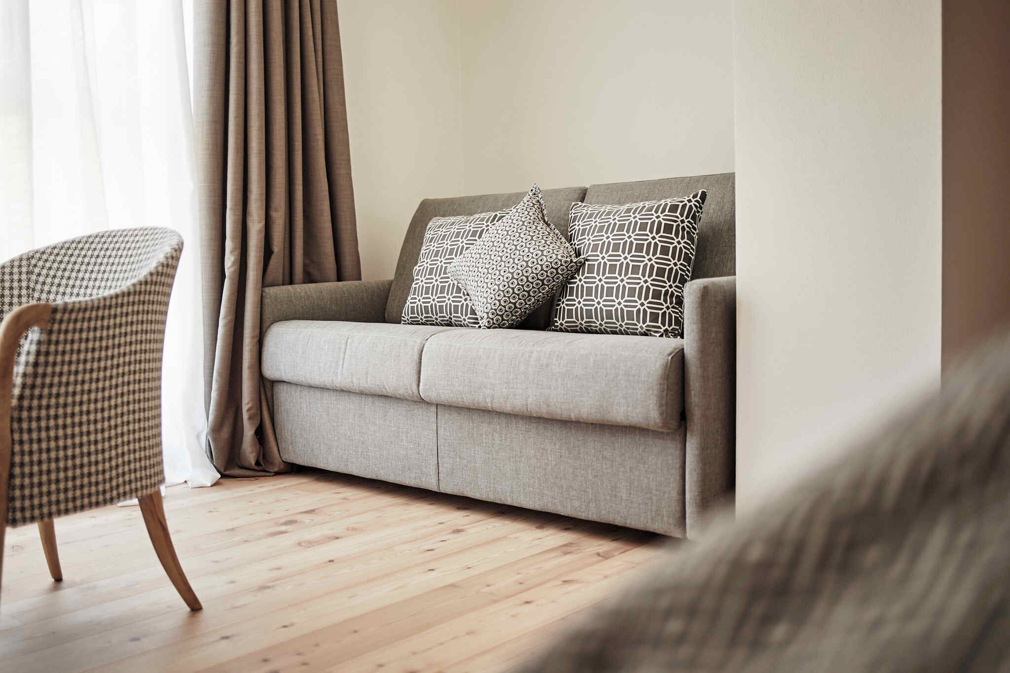 Una sala de estar con un sofá, almohadones estampados, un sillón a cuadros de piedritas y piso de madera.
