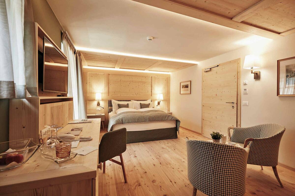 Une chambre d’hôtel confortable, avec un plancher en bois, un lit doté d’une tête de lit, un bureau avec une chaise et deux fauteuils.