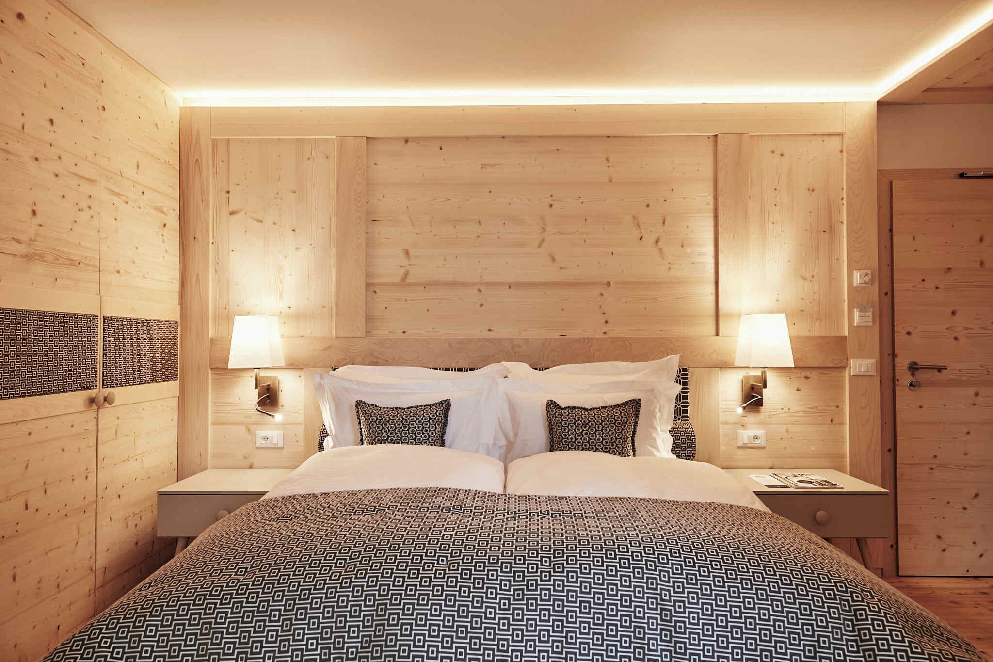 Ein Zimmer mit Holzwänden, einem Bett, zwei Nachttischlampen und einer Tür.