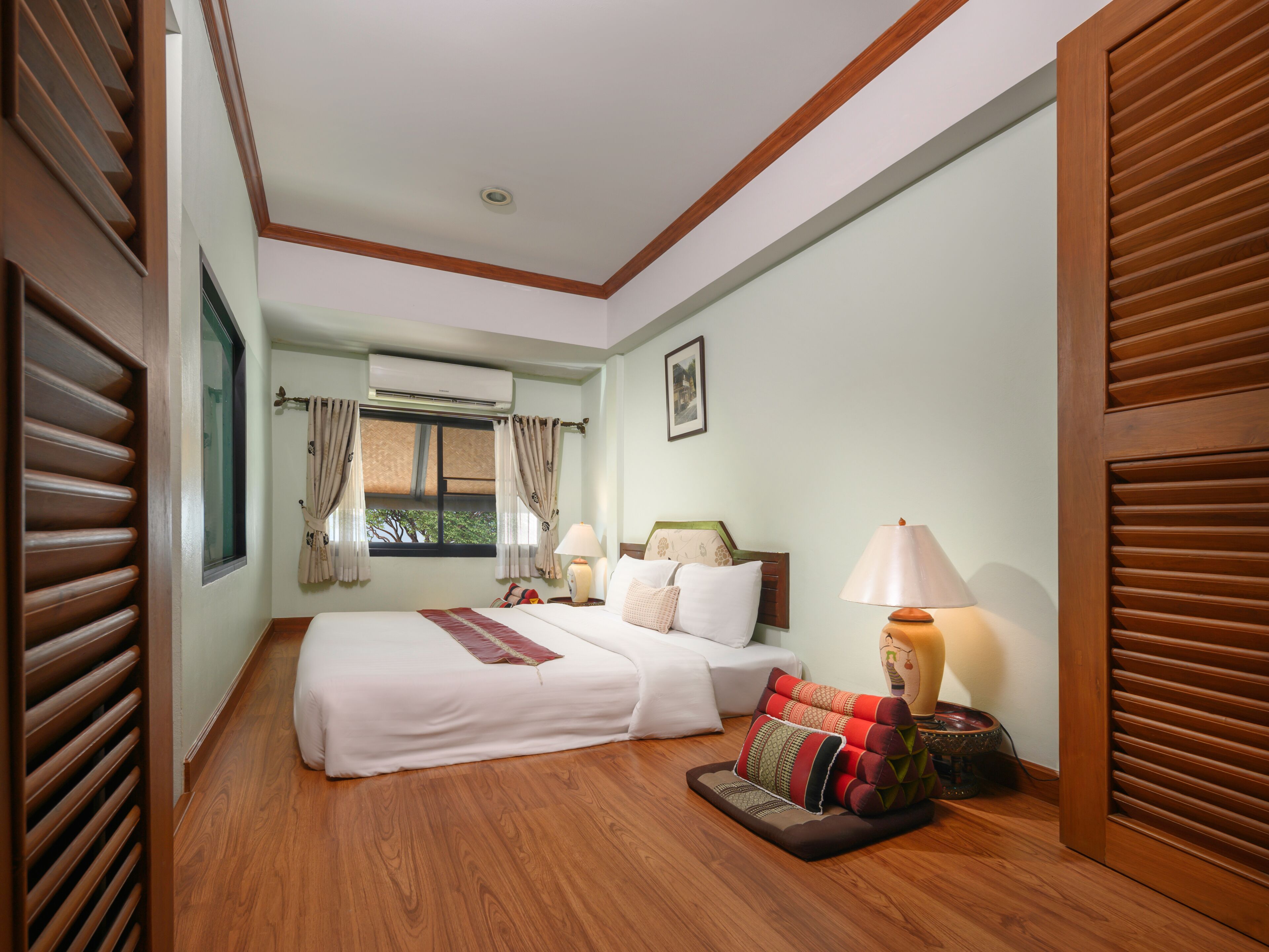 A hotel room with two beds, a window with curtains, a bedside lamp, and a wooden floor.