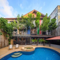 A swimming pool with a tiled deck, surrounded by a bamboo fence, and a building with a red roof and colorful vertical stripes.