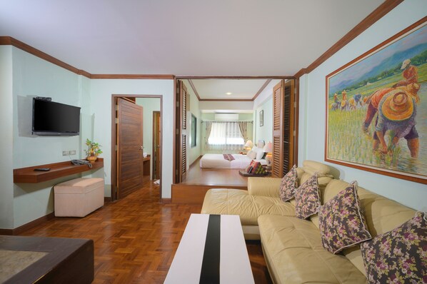 Habitación de hotel con piso de madera, un sofá color beige, un televisor de pantalla plana, un cuadro y una cama con vista al jardín.