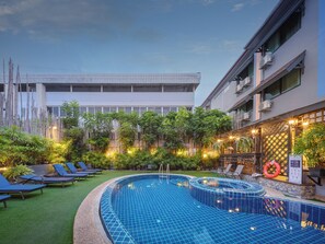A swimming pool with a tiled edge, surrounded by lounge chairs and greenery, with a building in the background. - Estia Chiang Mai Boutique Hotel (Chiang Mai)