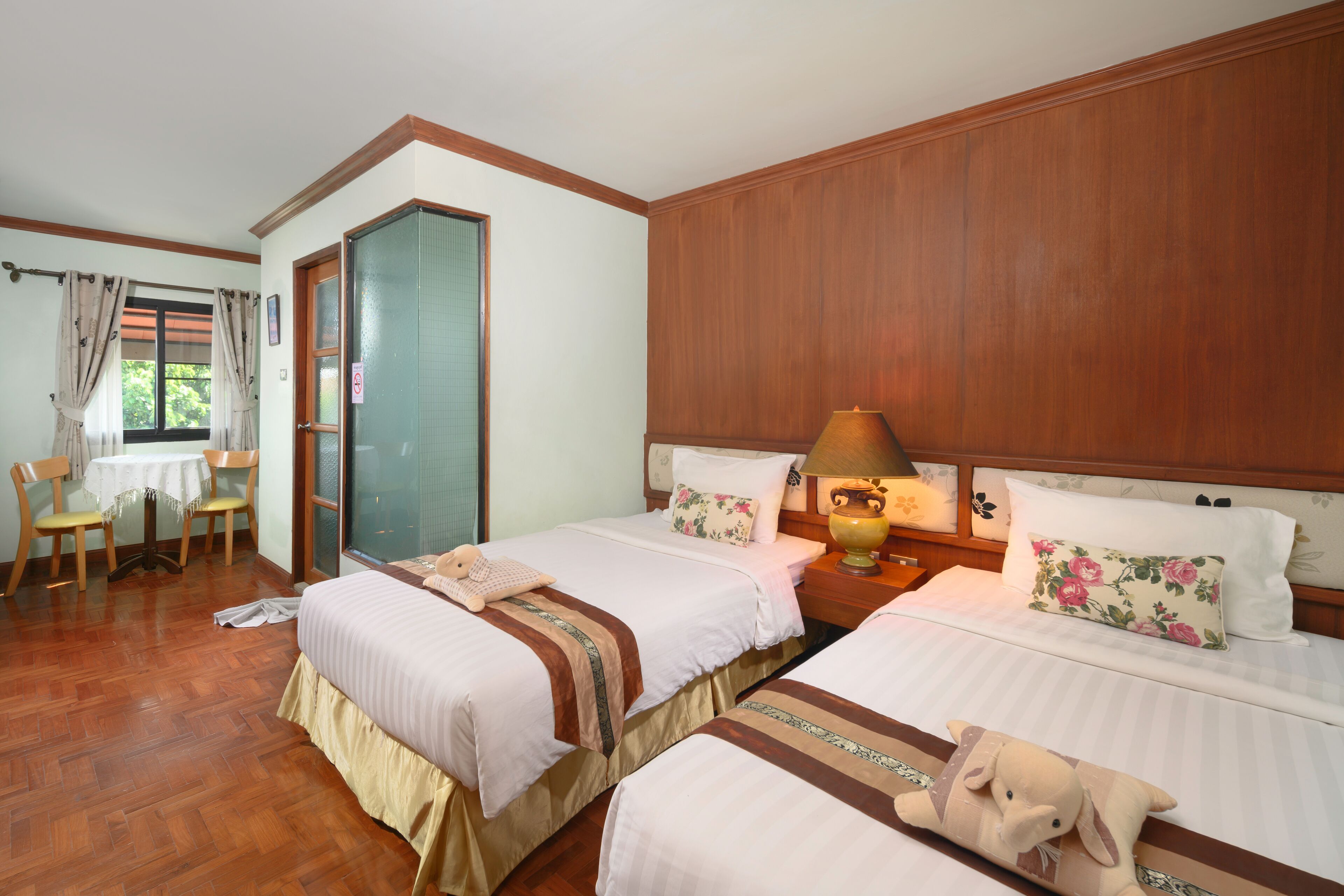 Une chambre d’hôtel avec deux lits, des lambris en bois aux murs, une petite table avec des chaises et une fenêtre avec des rideaux.