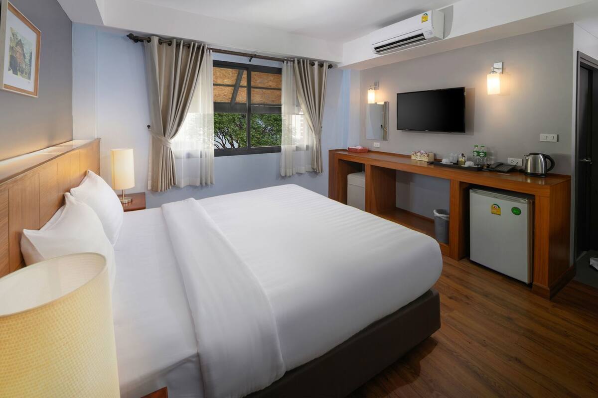 A hotel room with a large bed, a desk, a television, and a mini-fridge.