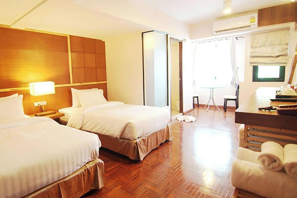 A hotel room with two beds, a desk, a chair, and a small table.