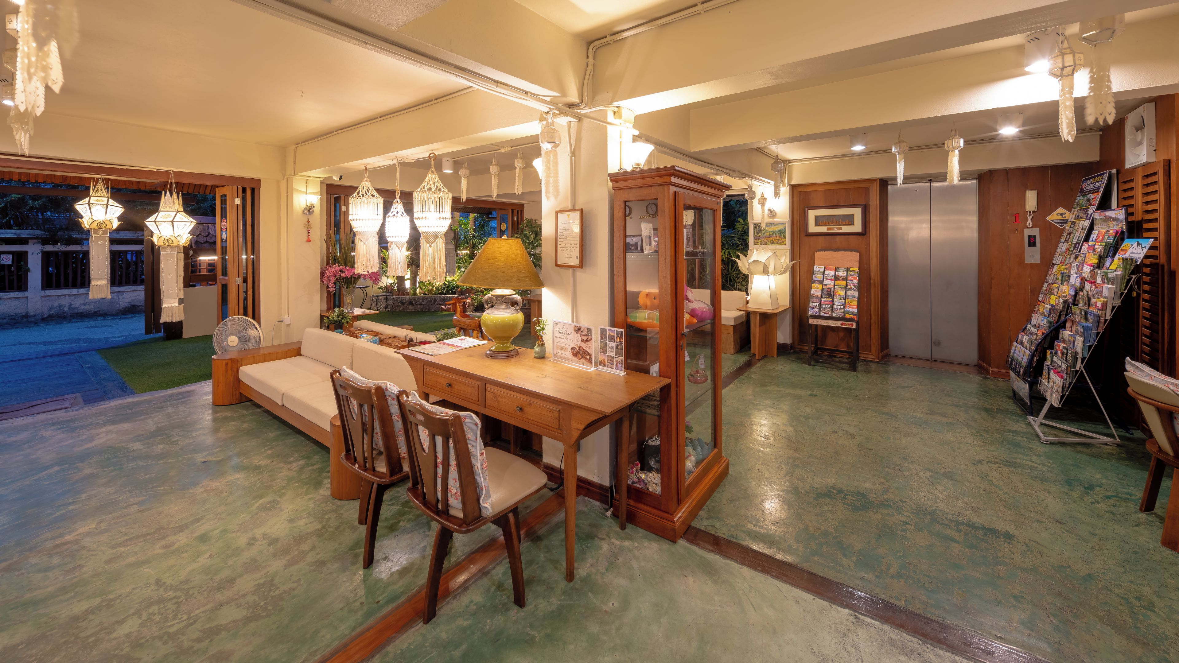A well-lit room with a wooden desk, a sofa, and a dining table. There are hanging lights and a lamp on the desk.