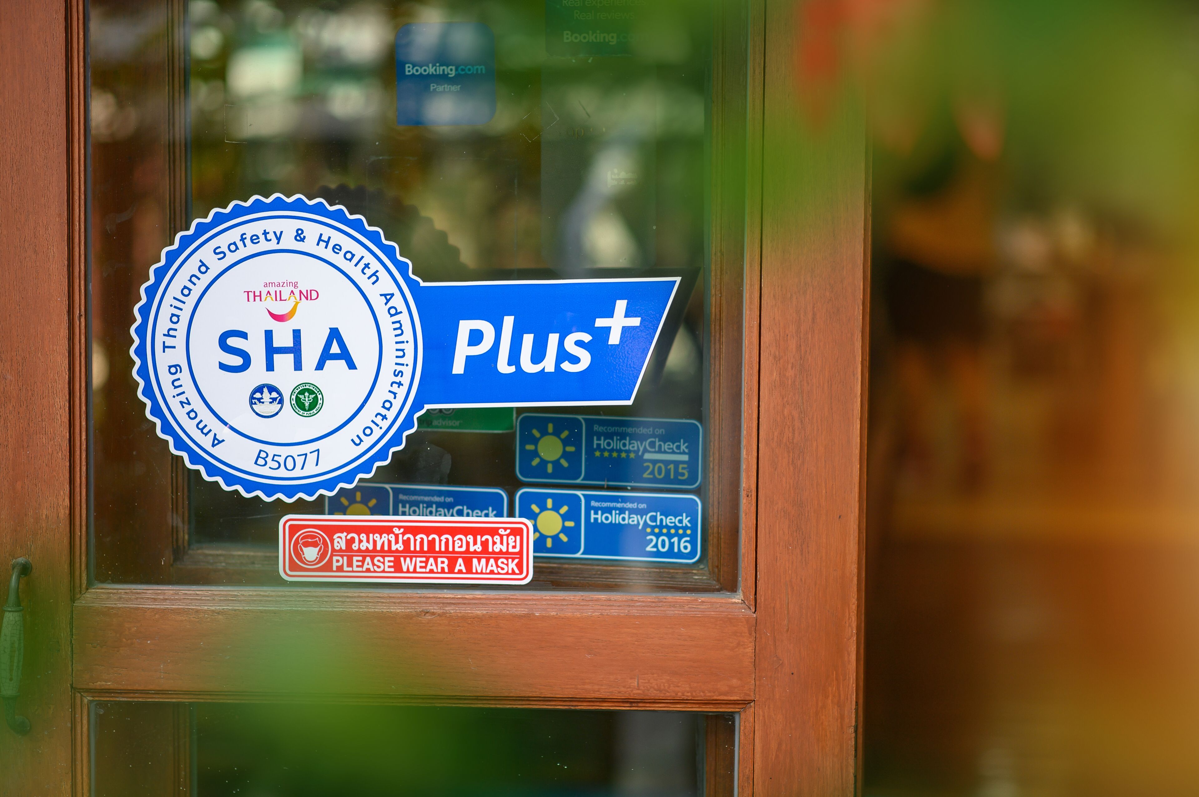 A window with a sticker indicating 'SHA Plus+' and a 'Please wear a mask' sign.