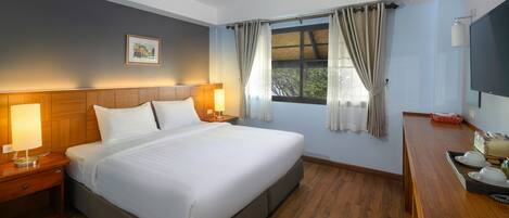A hotel room with a large bed, wooden headboard, bedside lamps, a flat-screen TV, and a window with curtains.