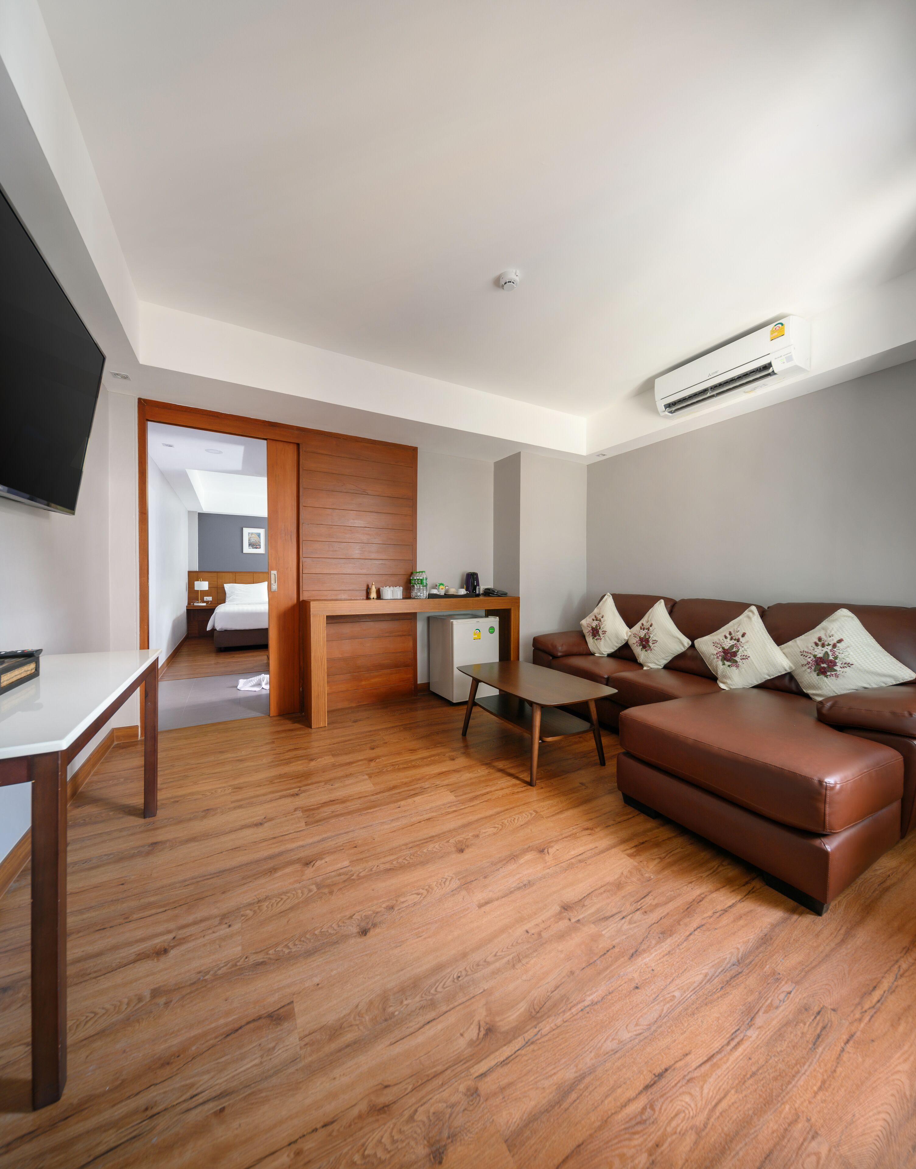 A modern living room with a brown leather sofa, a wooden coffee table, and a TV mounted on the wall.