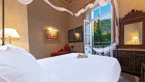 A bedroom with a large bed, a red bench, a window with a view of greenery, and a mirror. - Nafsimedon Hotel (Nafplio)
