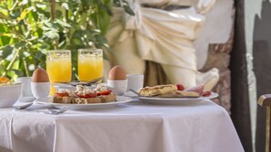 A table set with breakfast items, including toast, eggs, and orange juice, in front of a statue. - Nafsimedon Hotel (Nafplio)