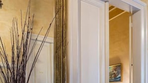A room with a large mirror, a vase with branches and flowers, and a bed with a painting in the background. - Nafsimedon Hotel (Nafplio)