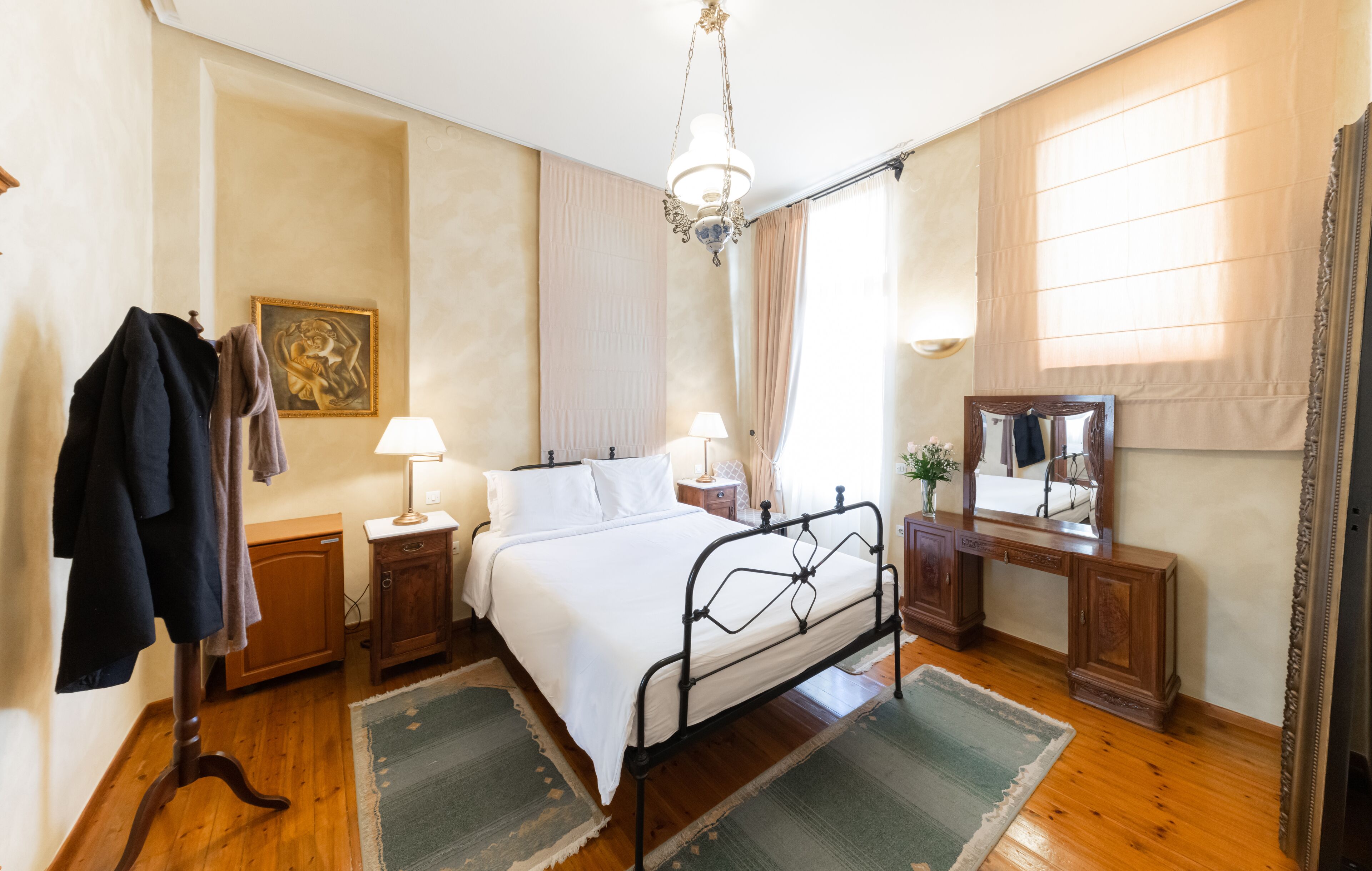 A bedroom with a bed, bedside tables, a dresser, a mirror, and a hanging coat rack.