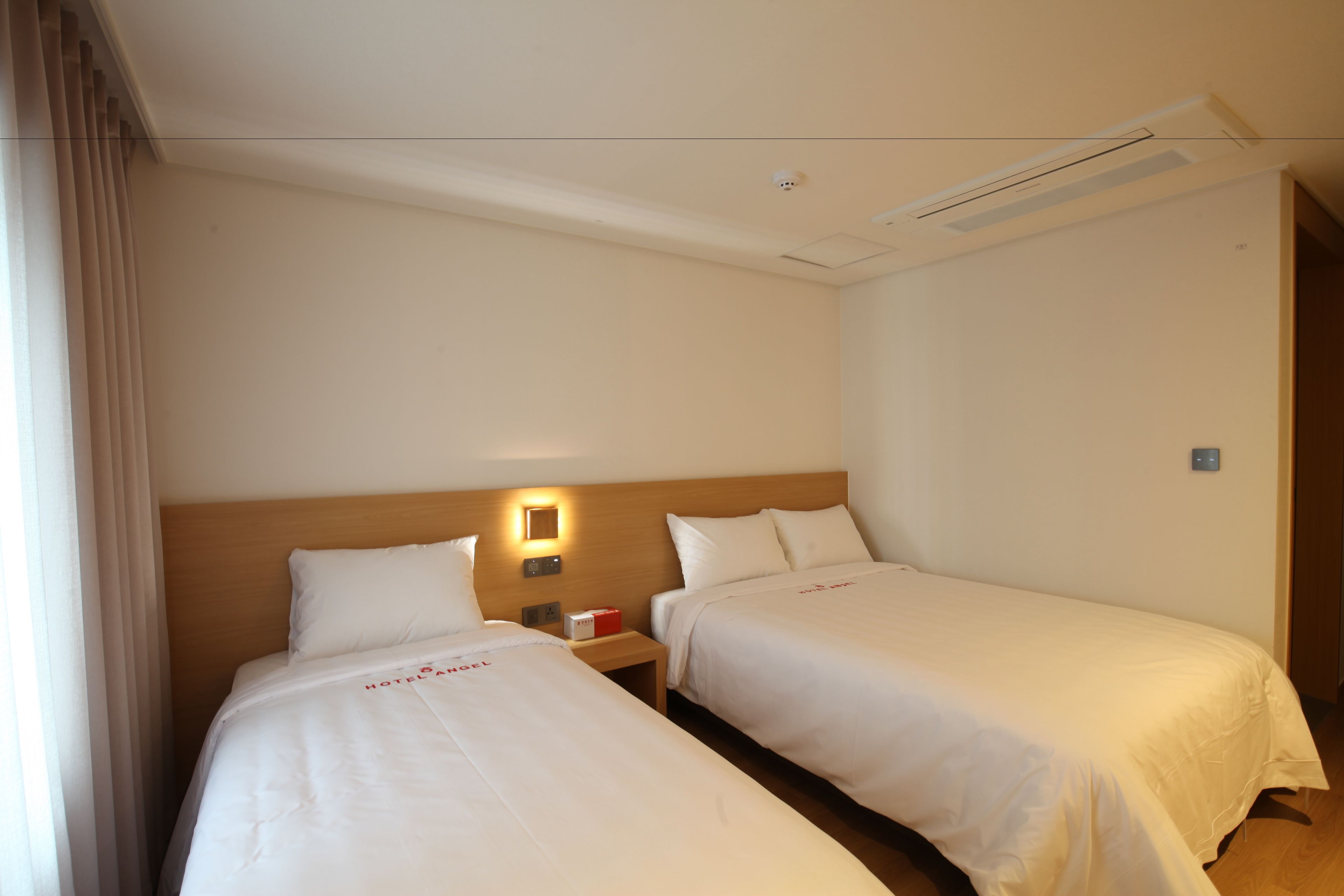 A hotel room with two beds, a nightstand, and a wall-mounted light.