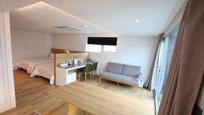 Een moderne, compacte kamer met een bed, een bureau, een bank en een eethoek.