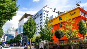 Een modern gebouw met een opvallend 'NC'-bord, omringd door bomen en andere gebouwen.